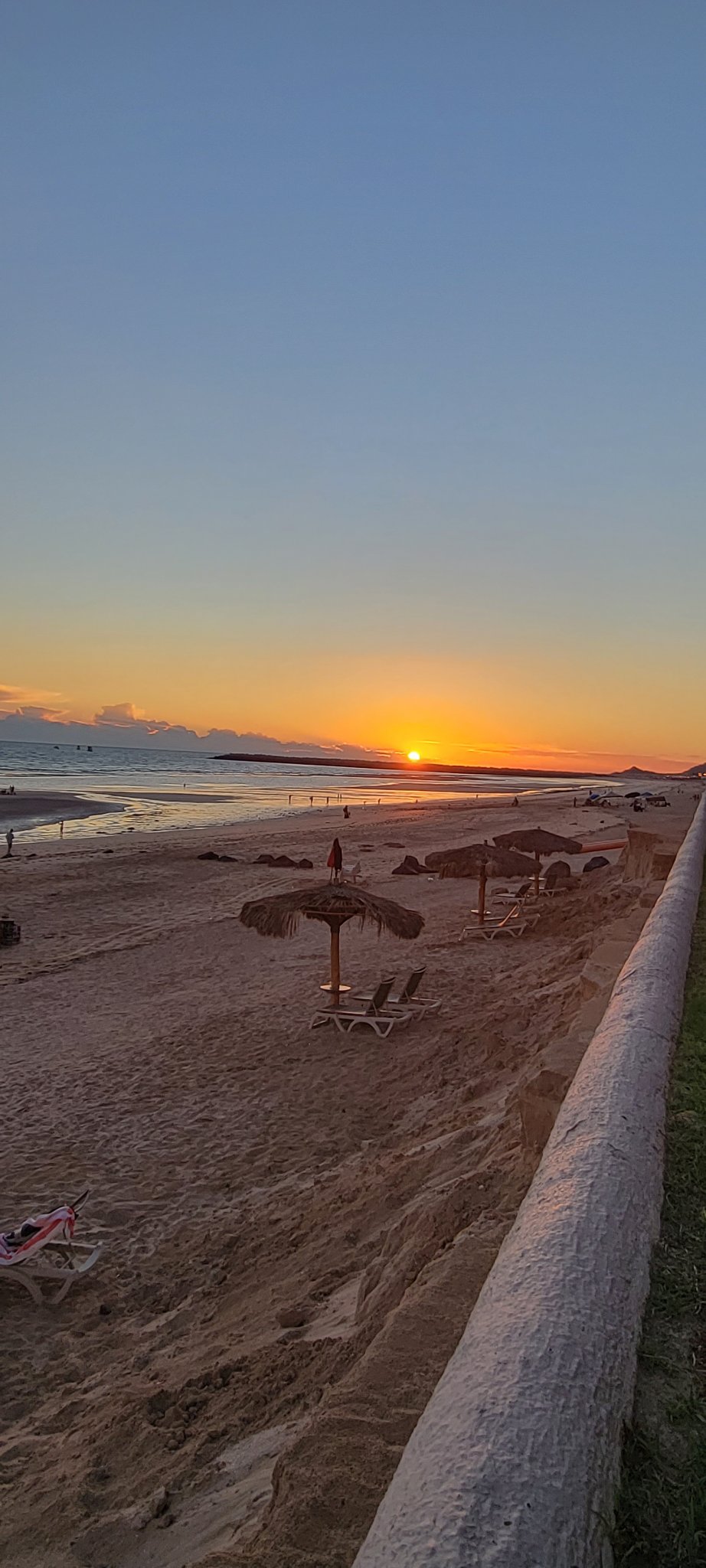 Sun setting beyond the beach, palapa and lounge chairs