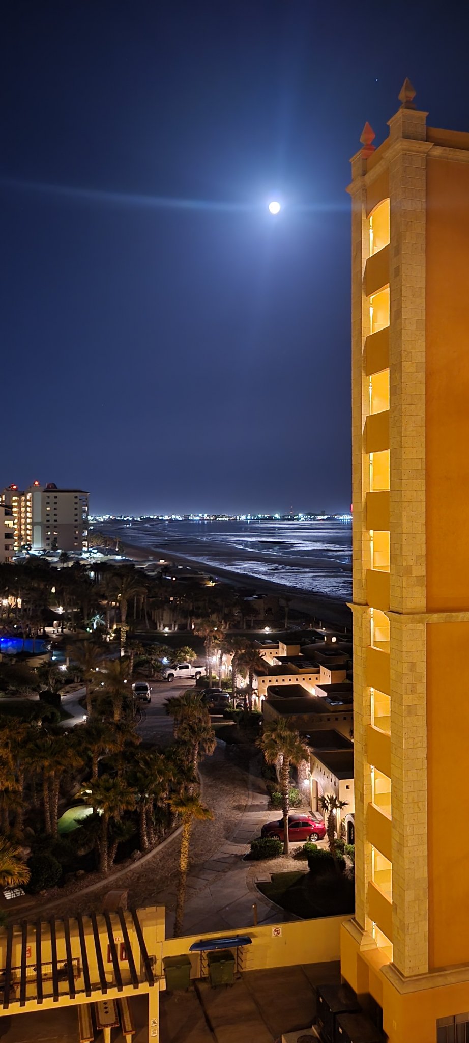 Moon shining over the nighttime ocean beside an illuminated resort tower