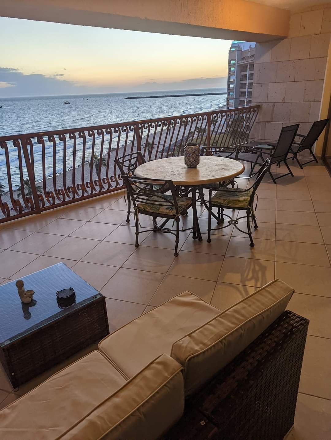 Large furnished balcony with dining table and direct ocean view at dusk