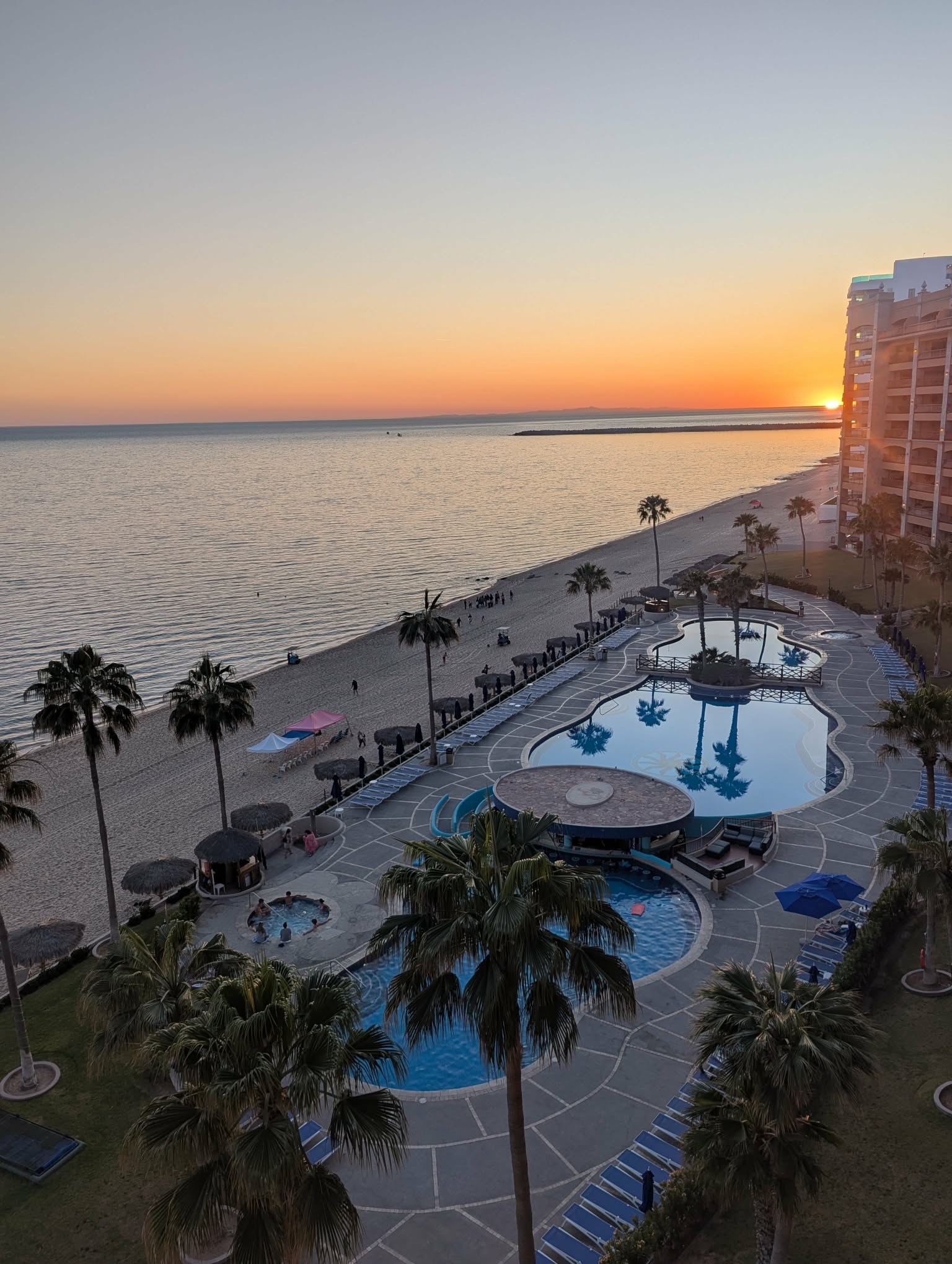 Resort pools reflecting palm trees at sunset beside the beach